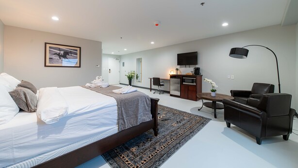 Ein modernes Hotelzimmer mit einem großen Bett, einem Schreibtisch, einem Sessel und einem Fernseher.
