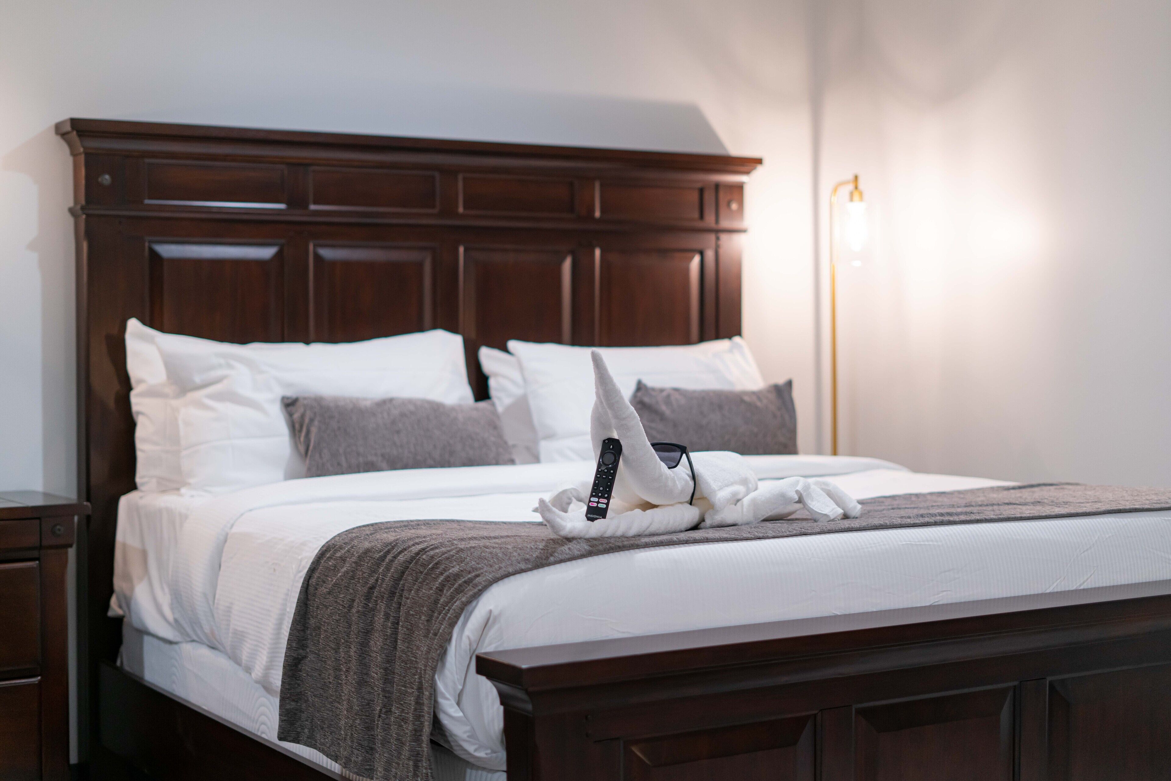 A neatly made bed with a wooden headboard, white and gray pillows, a blanket, and a remote control on the bed.