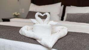 A neatly made bed with a towel arranged in the shape of swans on a gray bedspread.
