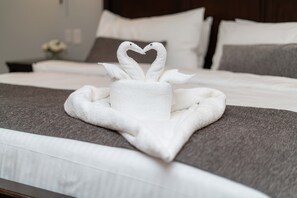 A neatly made bed with a towel arranged in the shape of swans on a gray bedspread.