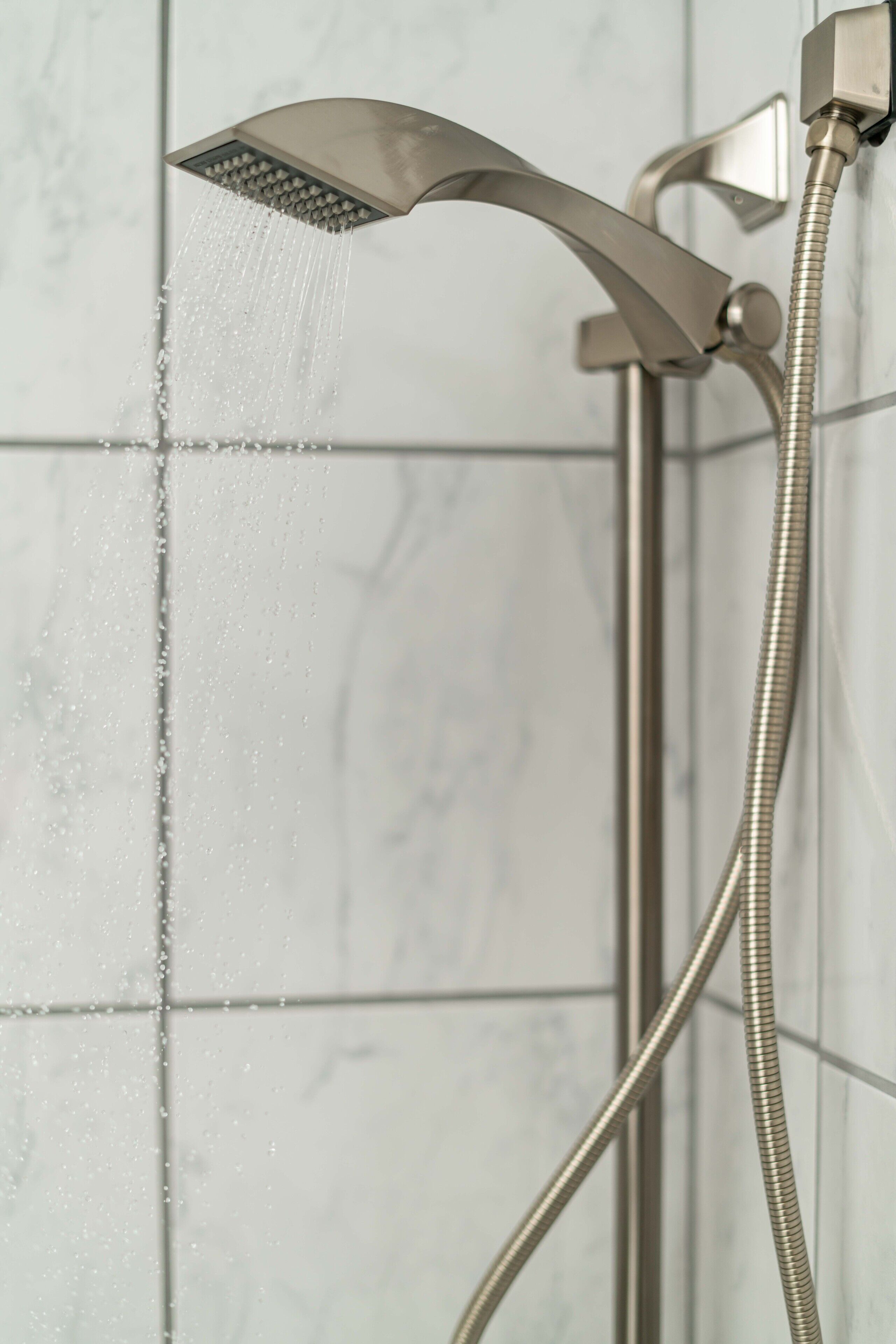 A modern showerhead with a flexible hose, mounted on a wall with a tiled background.
