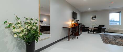 A modern hotel room with a large mirror, a desk with two chairs, a television, and a large window.