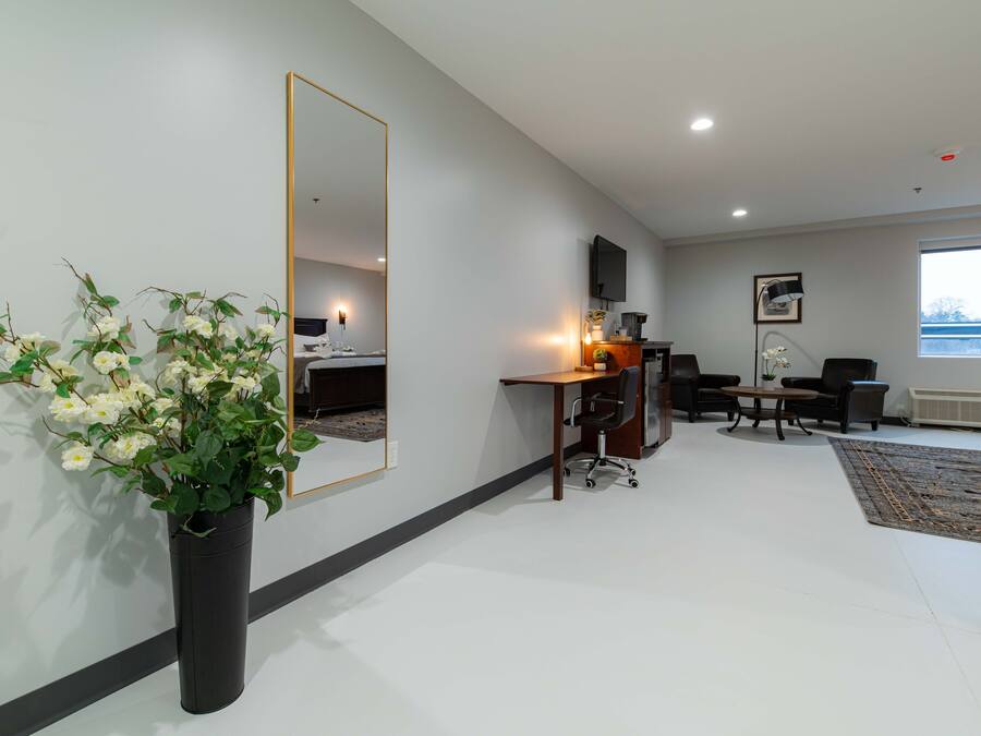 A modern hotel room with a large mirror, a desk with two chairs, a television, and a large window.