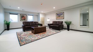 Ein geräumiges Wohnzimmer mit zwei Ledersofas, einem Couchtisch und einem großen Teppich. Zwei Topfpflanzen, ein gerahmtes Bild von einem Pferd und ein Spiegel sind an der Wand zu sehen.