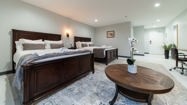 A hotel room with two beds, a round wooden table, a potted orchid, and a painting on the wall.