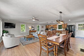 Un vaste espace de vie comprenant une table à manger, des chaises en bois, un canapé et un ventilateur de plafond.