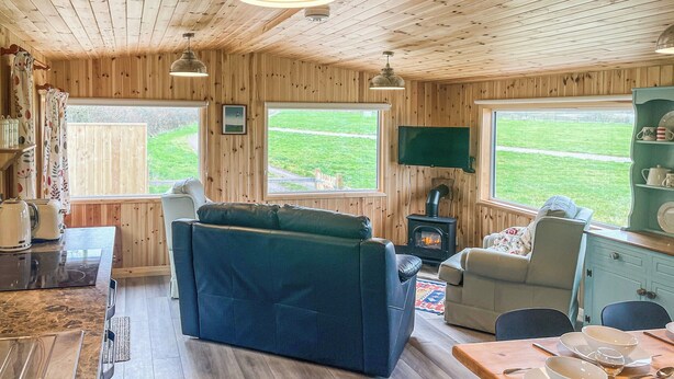 Interior acogedor de una cabaña con sofá, mesa de comedor y estufa de leña.