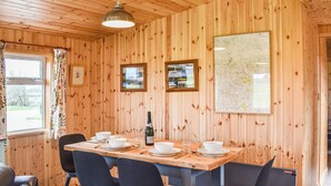 Una habitación con paneles de madera, con una mesa de comedor lista para cuatro personas, que incluye una botella de champán, cuencos blancos y sillas negras.