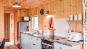 Cocina con paneles de madera, un fregadero, estufa y tostadora. Hay armarios, un reloj y una ventana.