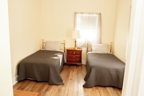 A small, clean room with two single beds, a nightstand with a lamp, and a window with sheer curtains. - Condos at Fairlawn (Poland)