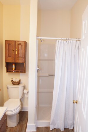 A bathroom with a toilet, a wooden cabinet with a bottle, and a shower curtain. - Condos at Fairlawn (Poland)