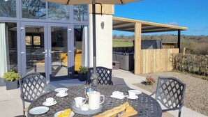 Eine Terrasse im Freien mit einem runden Tisch, gedeckt für das Frühstück, einschließlich Tellern, Tassen und einem heißen Getränk.