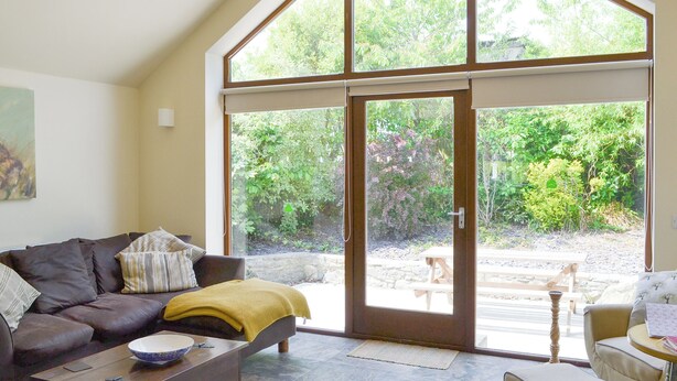 A living room with a sofa, coffee table, and a view of a garden through a large sliding glass door. - 2 bedroom accommodation in Llanfachraeth, near Holyhead (Llanfachraeth, near Holyhead)