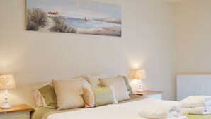 A neatly made bed with pillows, a bedside lamp, and a painting of a beach scene on the wall. - 2 bedroom accommodation in Llanfachraeth, near Holyhead (Llanfachraeth, near Holyhead)