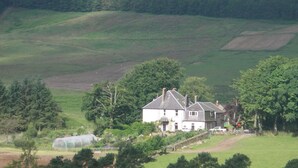 Une maison de campagne dotée d’un grand jardin, entourée de collines douces et d’une zone boisée.