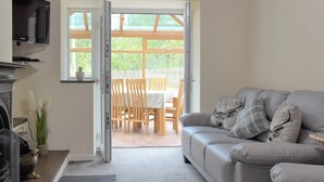 Una sala de estar con un sofá gris, televisor, chimenea y vistas a un patio exterior con mesa y sillas.