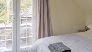 Un dormitorio con cama, ventana con cortinas y vistas al exterior.