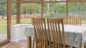 Un invernadero con mesa y sillas, ventanas amplias y vista a un jardín.