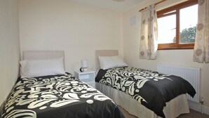 A twin room with two beds, each with a headboard, bedside tables, and lamps. There is a window with curtains and a radiator below. - 3 bedroom accommodation in Llansteffan (Llansteffan)