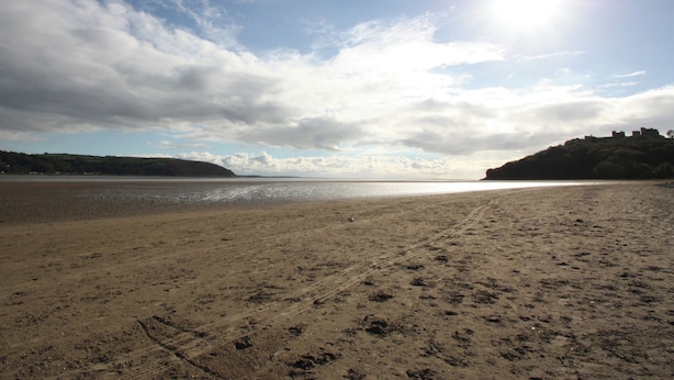 A beach with a clear sky, a calm sea, and a distant hill with structures. - 3 bedroom accommodation in Llansteffan (Llansteffan)