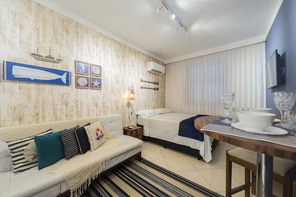 Quarto de hotel com parede de madeira, sofá, cama, mesa de jantar e televisão.