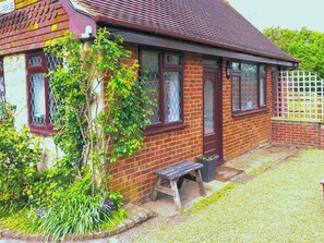 A brick house with a red roof, a wooden bench, and a small garden area.