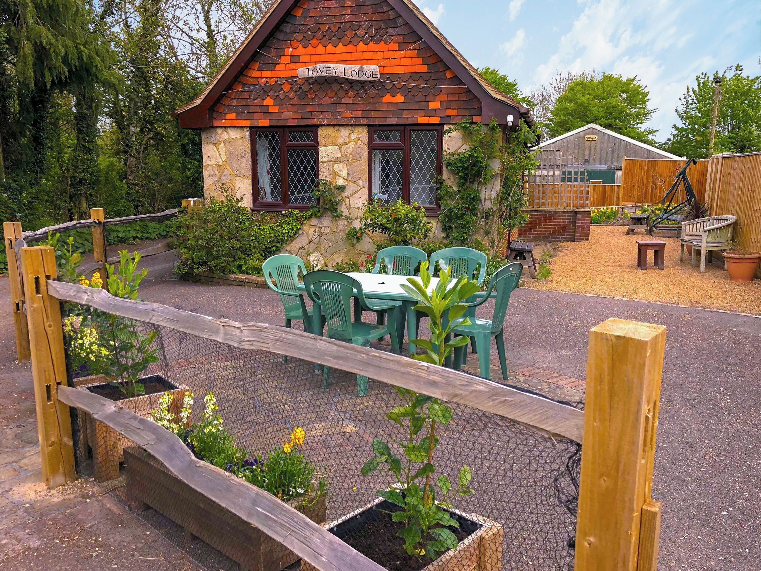 A rustic lodge with a stone facade, a wooden fence, and a table with chairs in front.