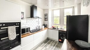 Une cuisine moderne avec des meubles blancs, une cuisinière noire, un four à micro-ondes, un évier et un réfrigérateur noir.