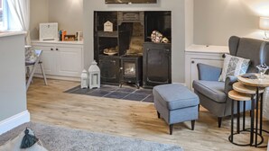 Una sala de estar moderna con chimenea, televisor de pantalla plana montado encima y un espacio de descanso cómodo con sofá y reposapiés.
