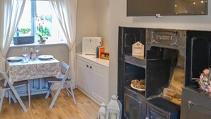 Un comedor con una mesa dispuesta para dos personas, una ventana con cortinas, un armario blanco y un horno negro con un letrero que dice “HOME Sweet HOME”.