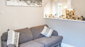 Un sofá gris con cojines estampados en una habitación con una zona de cocina visible a través de un vano abierto.