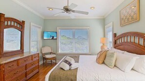 A bedroom with a bed, a wooden dresser, a chair, a ceiling fan, and a window with blinds.