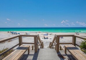 Un muelle de madera que conduce a una playa con aguas turquesas cristalinas y algunas personas a lo lejos.