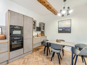 A modern kitchen with built-in ovens, a dining area with grey chairs, and a herringbone wooden floor.
