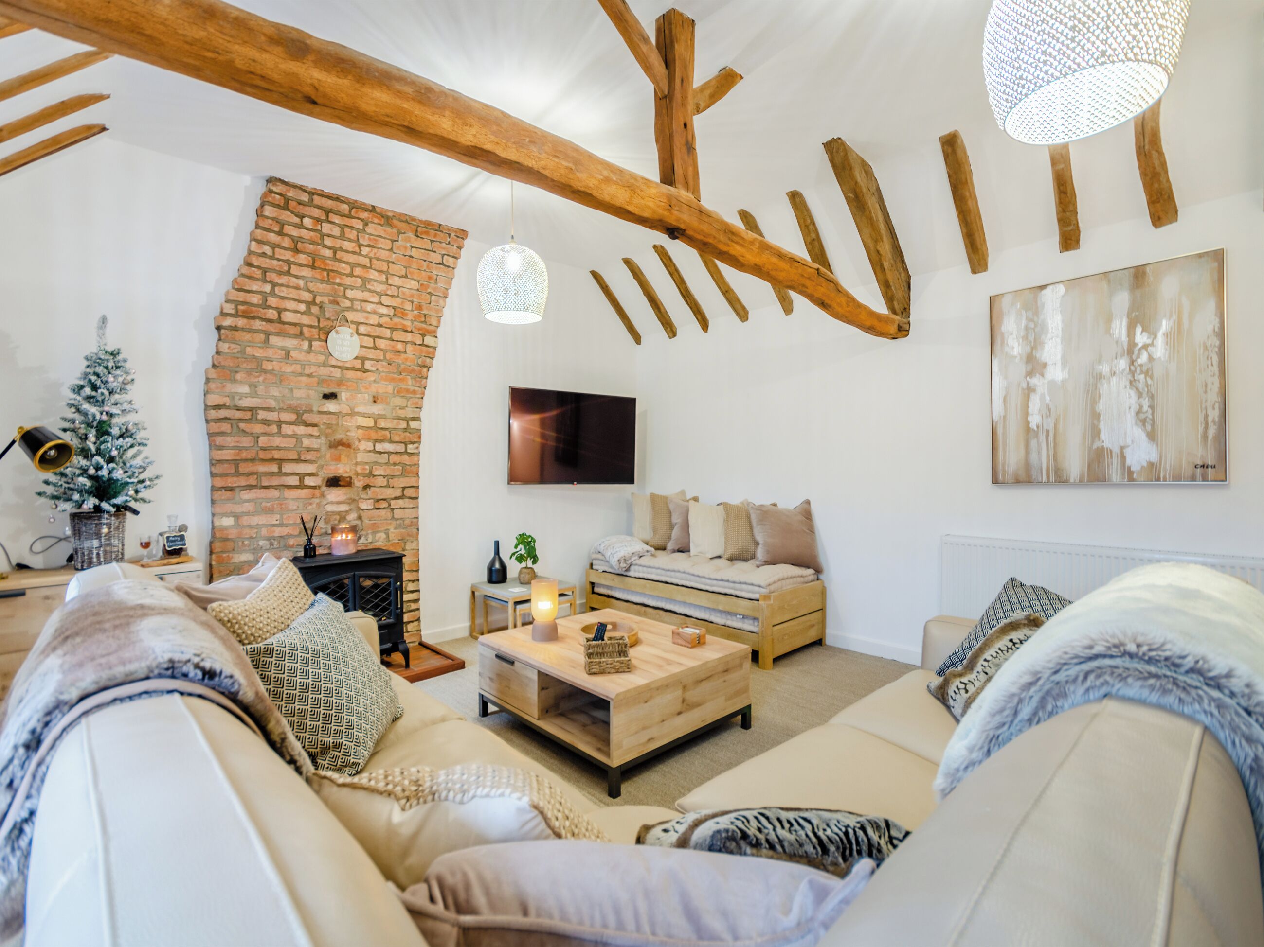 A cozy living room with a brick wall, wooden beams, a fireplace, a sofa, a coffee table, and a TV.