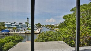 Uitzicht door een raam op een jachthaven met aanmerende boten, een vaarweg en moderne gebouwen op de achtergrond.
