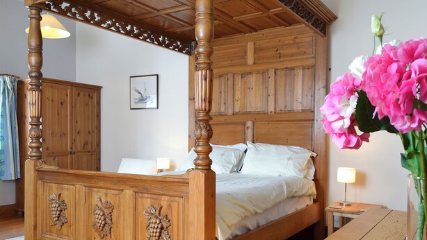 Una cama con dosel de madera con cuatro postes, una mesita de noche de madera y un jarrón con flores.