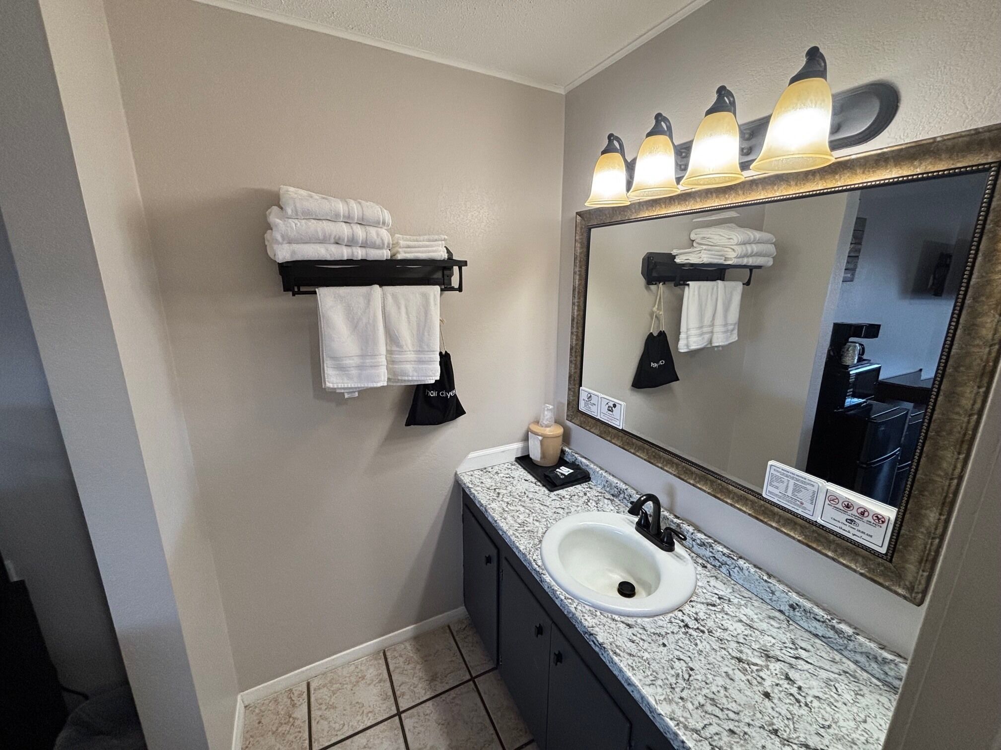 A bathroom with a sink, mirror, towel rack, and a towel dispenser.