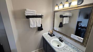 A bathroom with a sink, mirror, towel rack, and a towel dispenser.