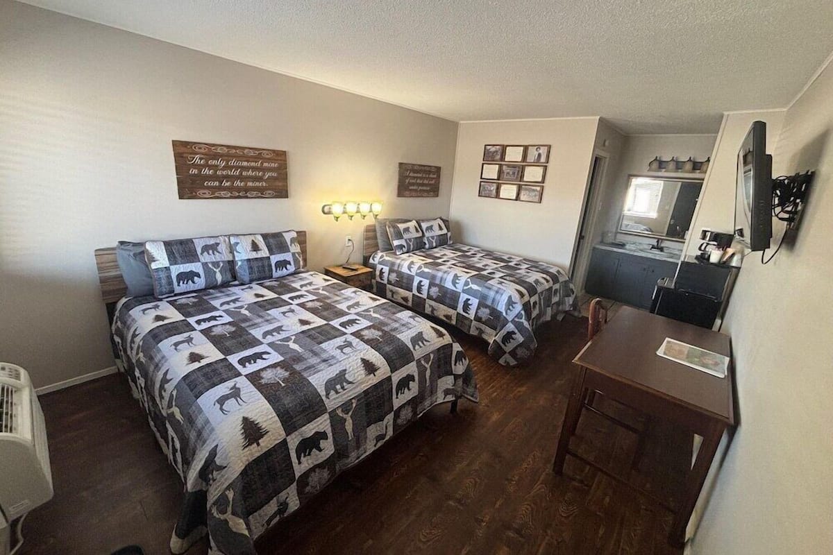 Quarto com duas camas, uma escrivaninha, um espelho e uma parede com certificados emoldurados.