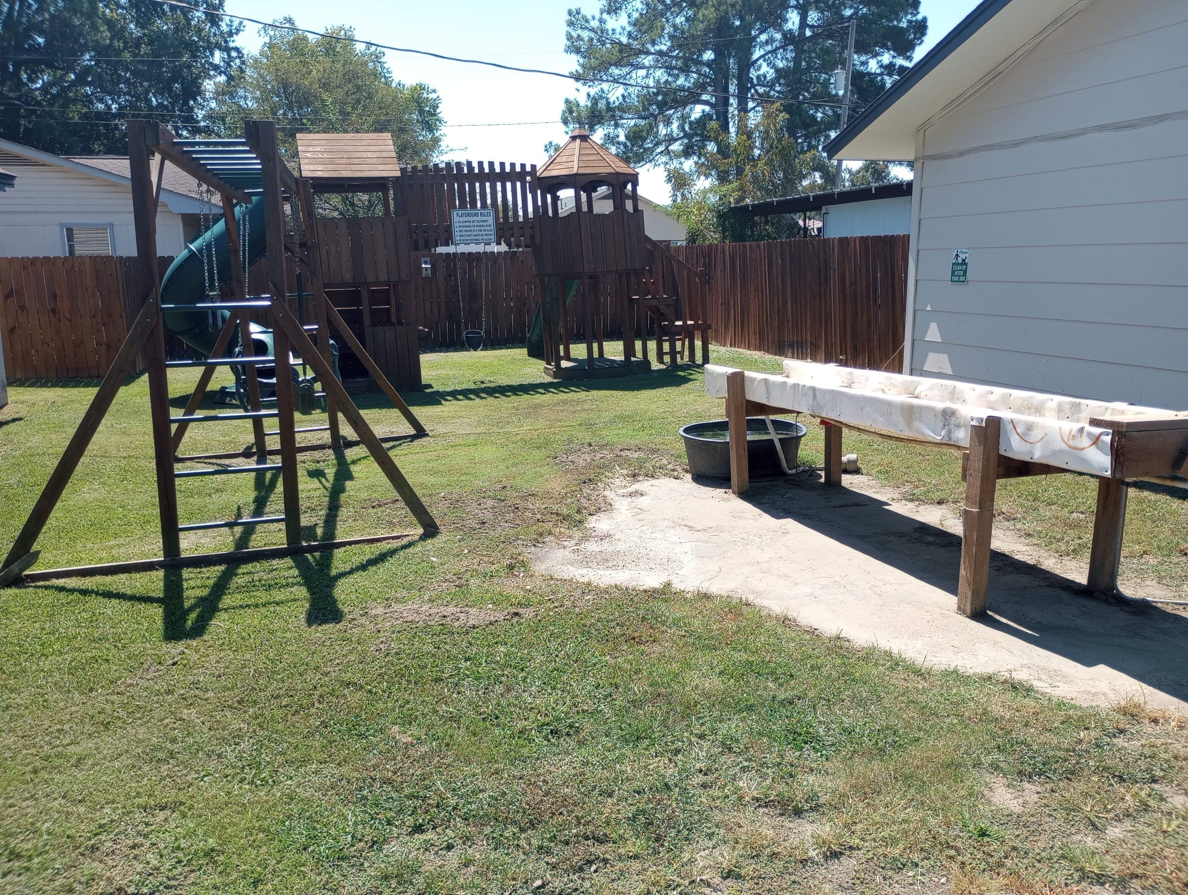 A fenced backyard with a swing set, a playhouse, and a bench.