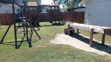 A fenced backyard with a swing set, a playhouse, and a bench.