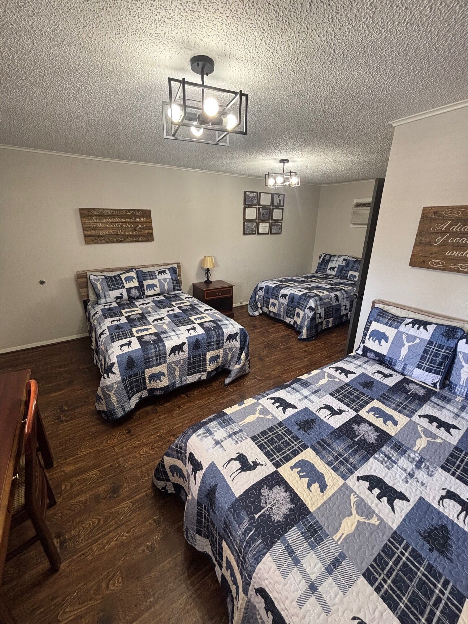 A bedroom with two beds, a wooden floor, a ceiling light fixture, and wall decorations.