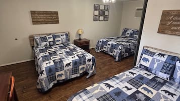 A bedroom with two beds, a wooden floor, a ceiling light fixture, and wall decorations.
