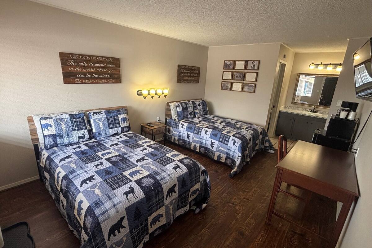 Quarto com duas camas, uma escrivaninha, um espelho e luminárias na parede.