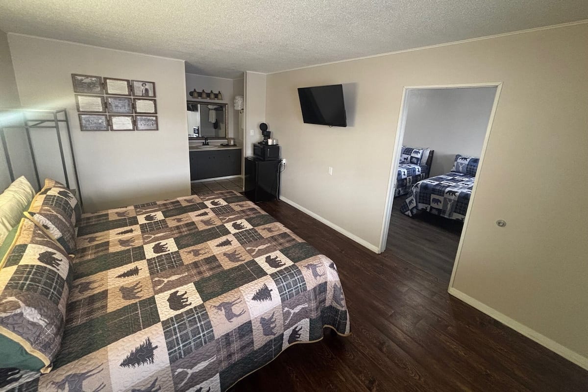 Quarto com cama, televisão, escrivaninha e banheiro ao fundo.