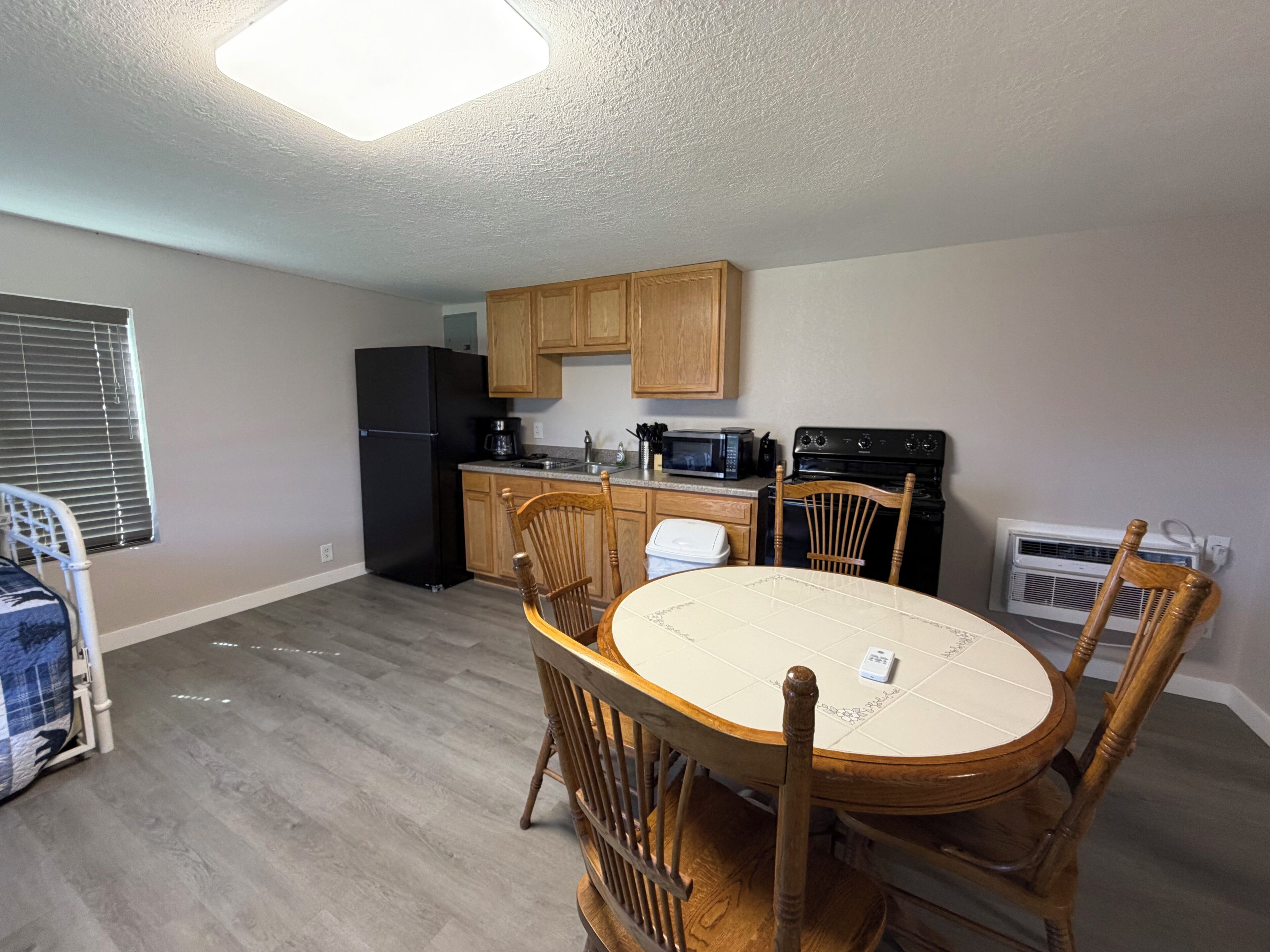 A compact kitchen with wooden cabinets, a black refrigerator, a microwave, a stove, and a dining table with chairs.