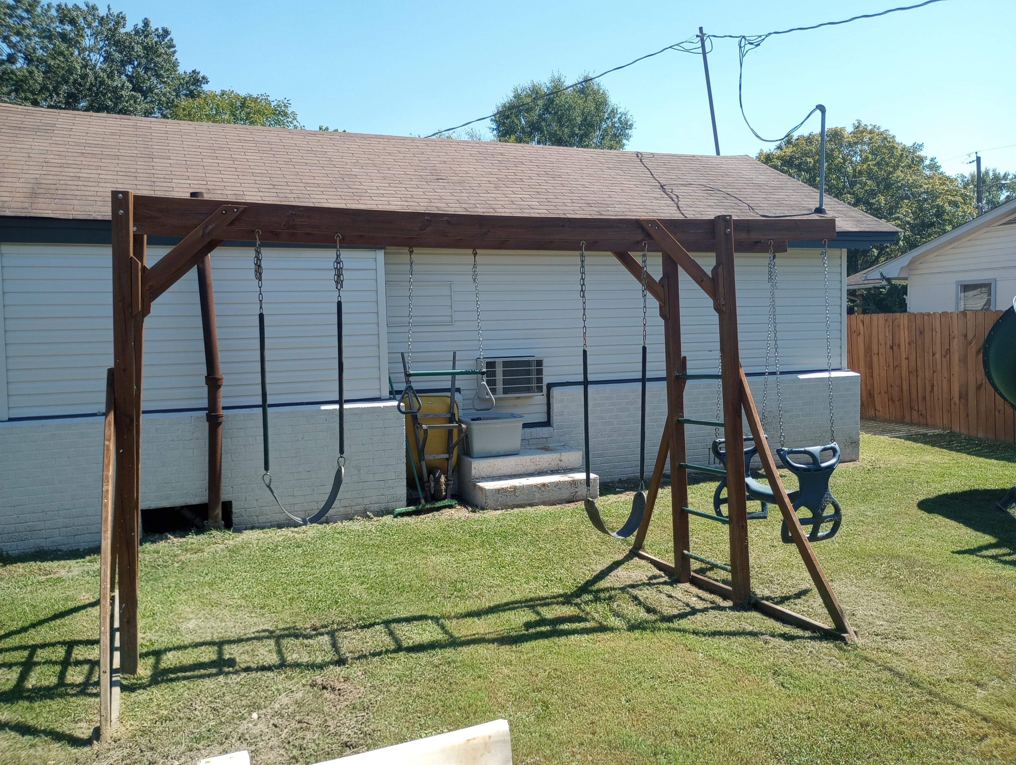 A backyard with a wooden swing set, a small play structure, and a house with a brown roof and white siding.