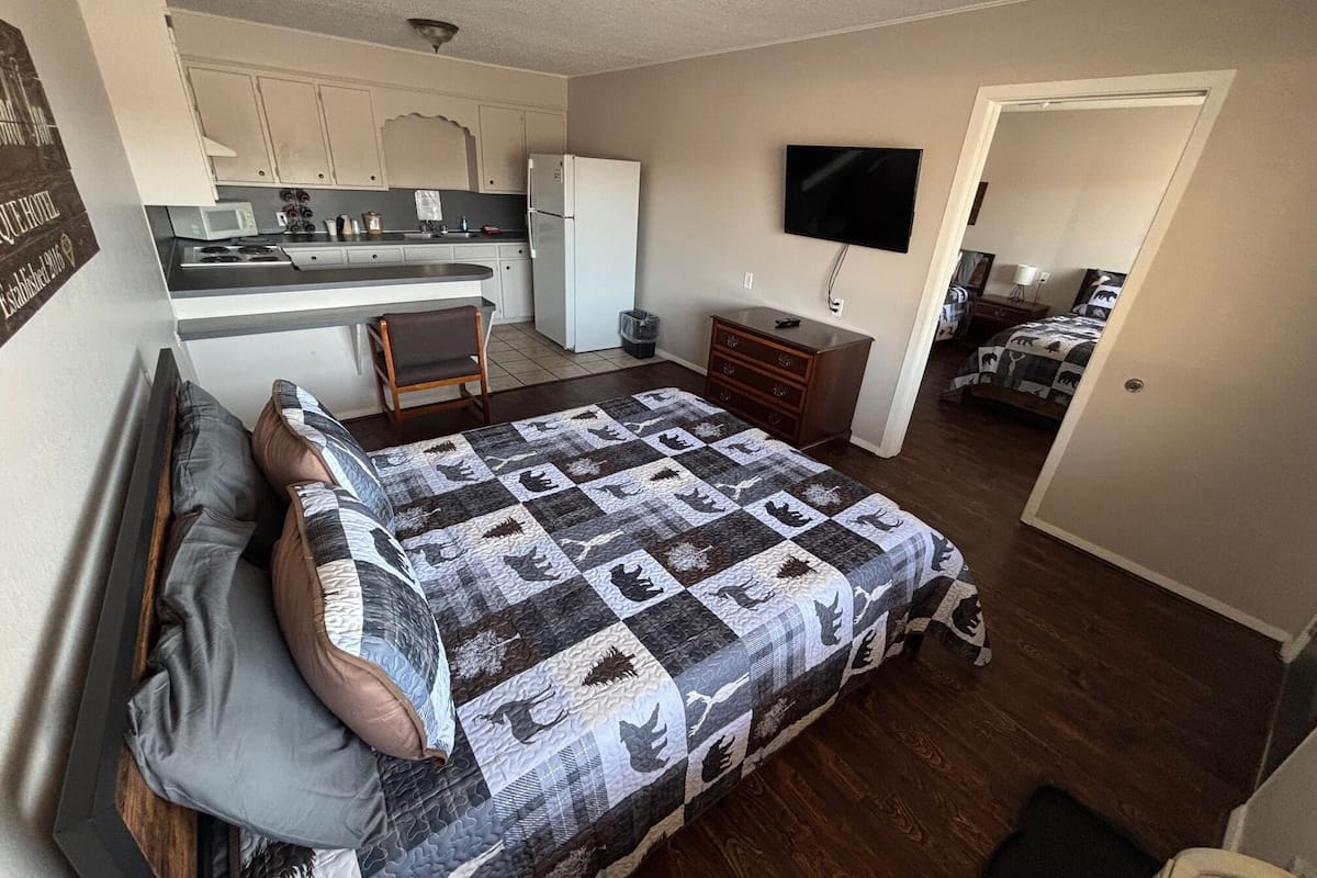 Quarto compacto com cama, escrivaninha pequena, televisão e cozinha compacta.