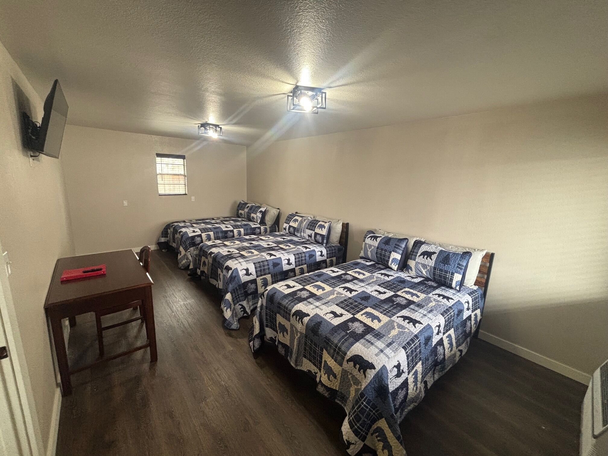 Quarto com três camas, uma escrivaninha e duas luzes no teto.